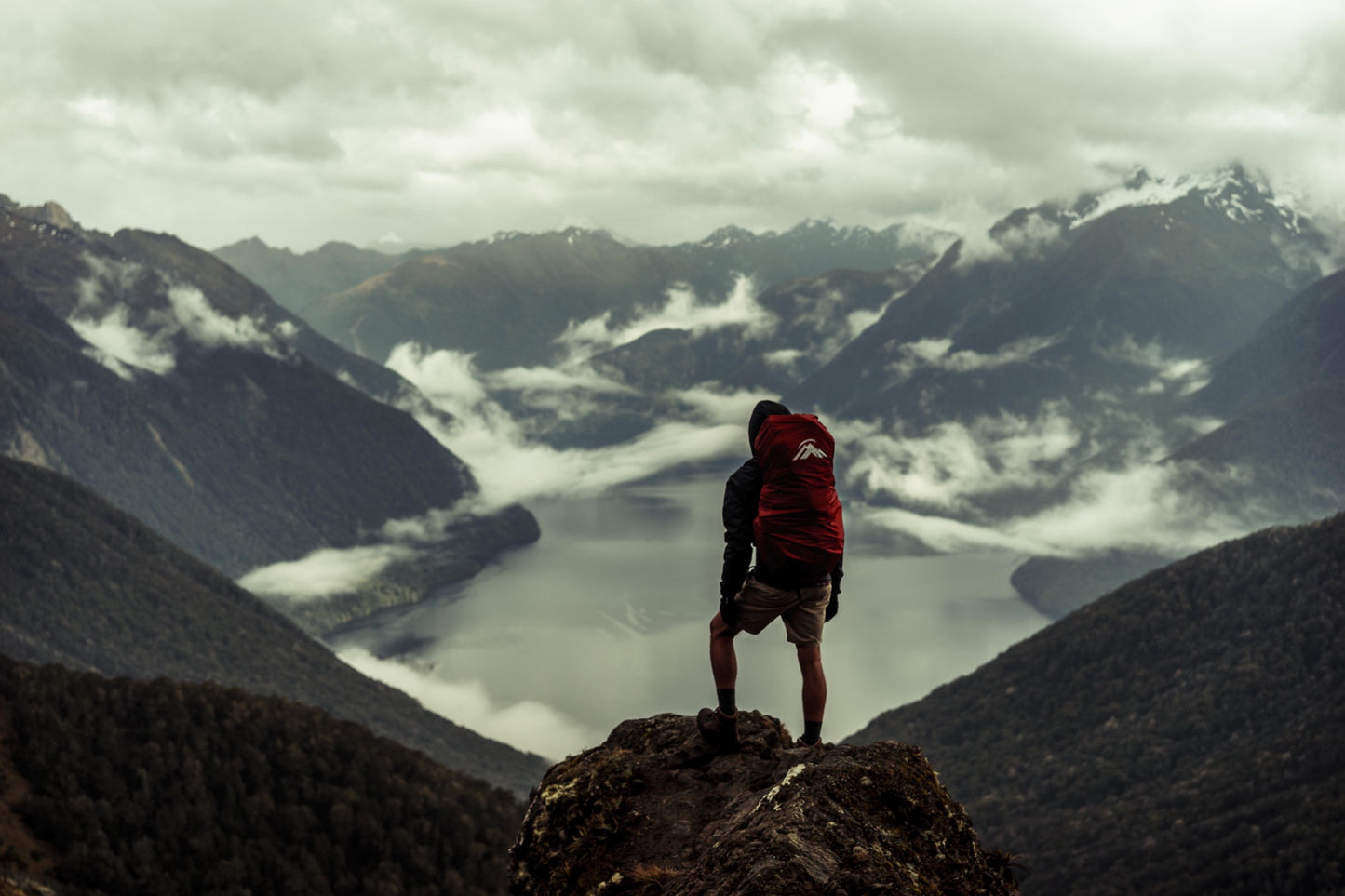 A hiker overlooks a body of water from a rocky outcrop in the mountains.