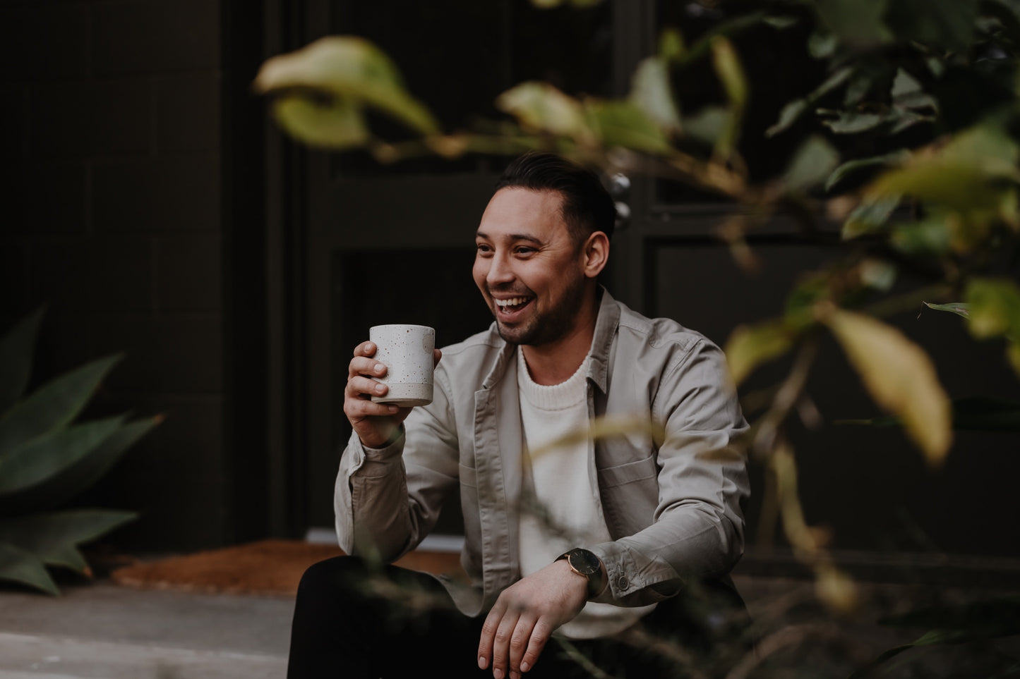 Charlie Wade enjoys a mug of coffee in a lush courtyard setting